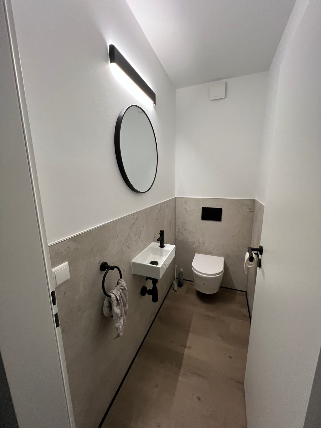 Gäste-WC mit halbhoch gefliester Wand, rundem Spiegel und schwarzen Armaturen